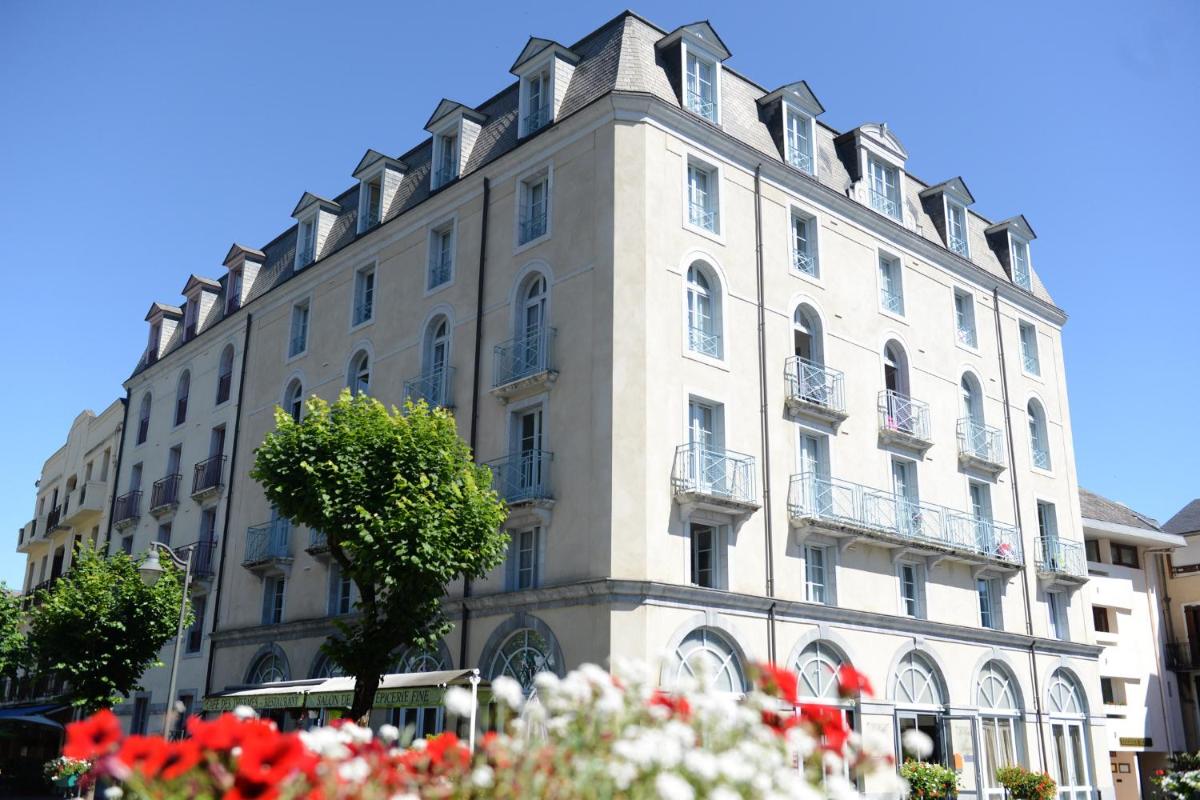 un grand bâtiment blanc avec des fleurs devant lui dans l'établissement La Résidence des Thermes, à Bagnères-de-Bigorre