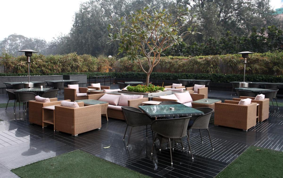 a patio with couches and tables and a tree at The LaLiT New Delhi in New Delhi