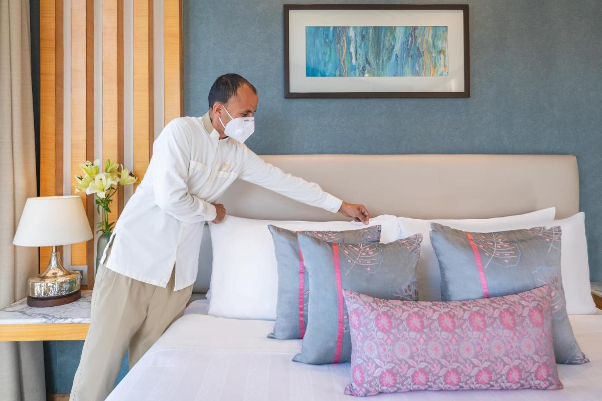 a man in a mask putting pillows on a bed at Welcomhotel by ITC Hotels, Shimla in Shimla
