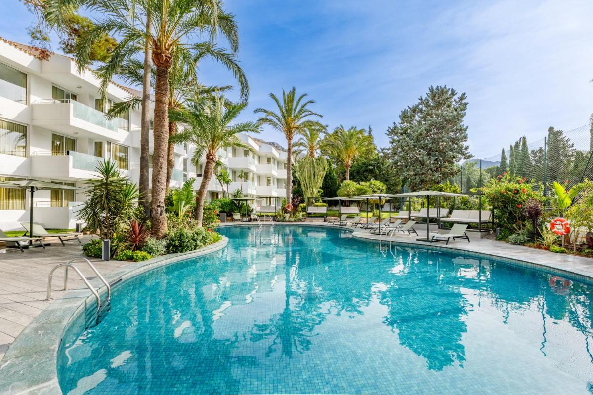 Una gran piscina con palmeras y condominios. en Hotel Illa d'Or & Club Apts 4* Sup, en Puerto Pollensa
