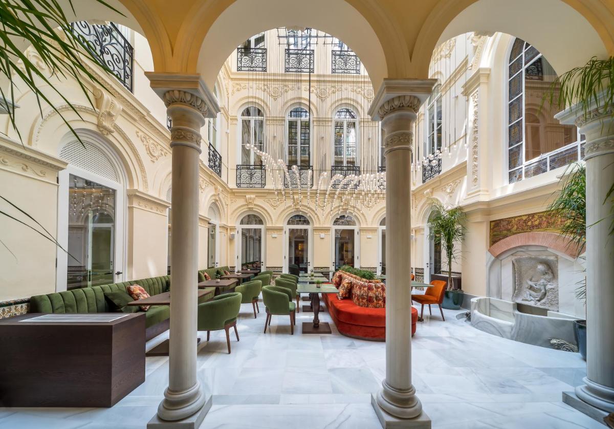 Un vestíbulo con mesas y sillas en un edificio. en Palacio Gran Vía, a Royal Hideaway Hotel, en Granada