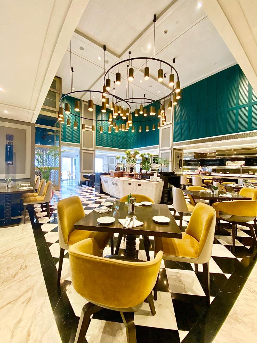 a restaurant with yellow chairs and tables and a chandelier at Taj Bengal in Kolkata