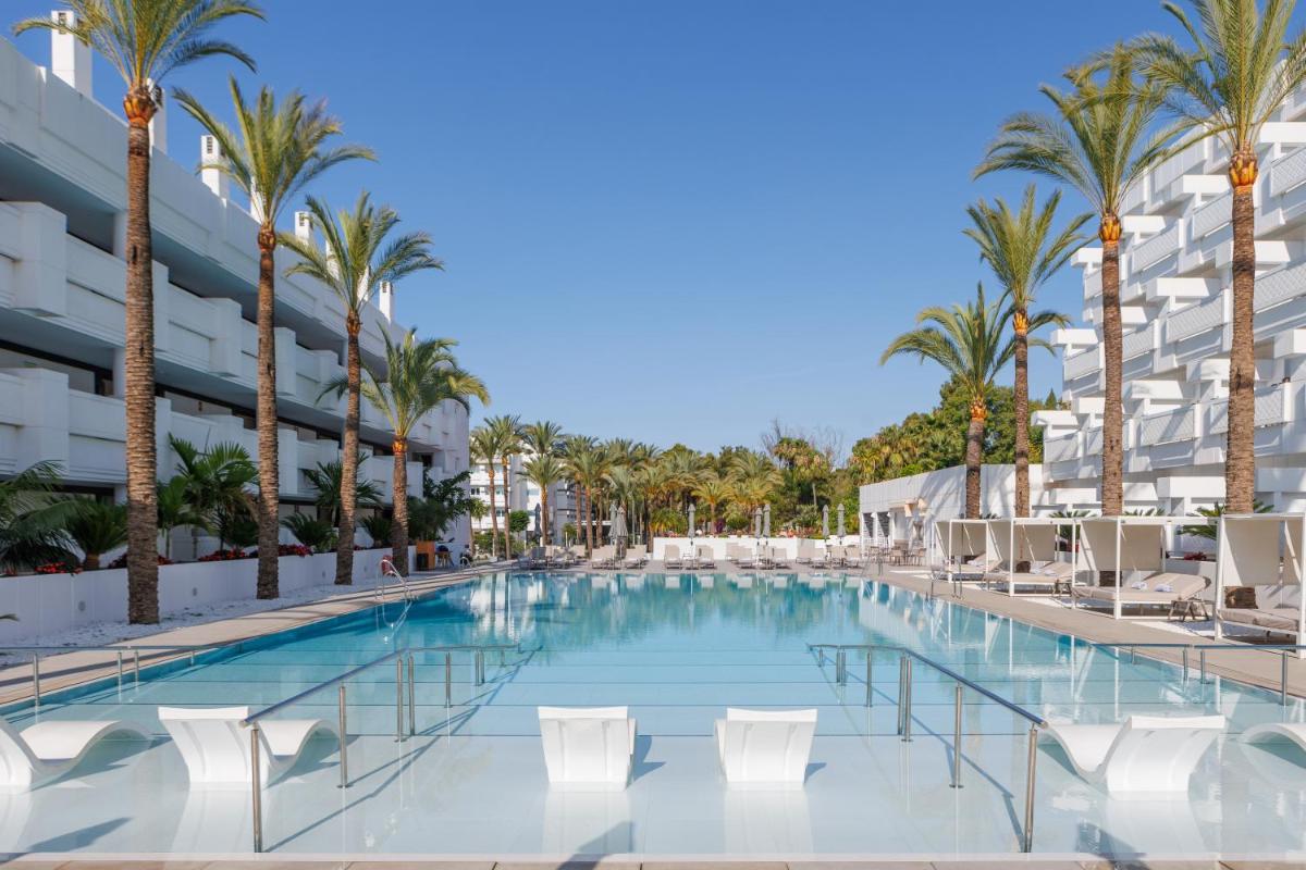 una piscina con sillas y palmeras frente a un edificio en Alanda Marbella Hotel & Wellness, en Marbella