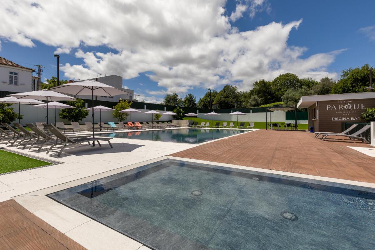 uma piscina com cadeiras e guarda-sóis ao lado de um prédio em Hotel Do Parque - Congress & SPA nas Termas de São Pedro do Sul