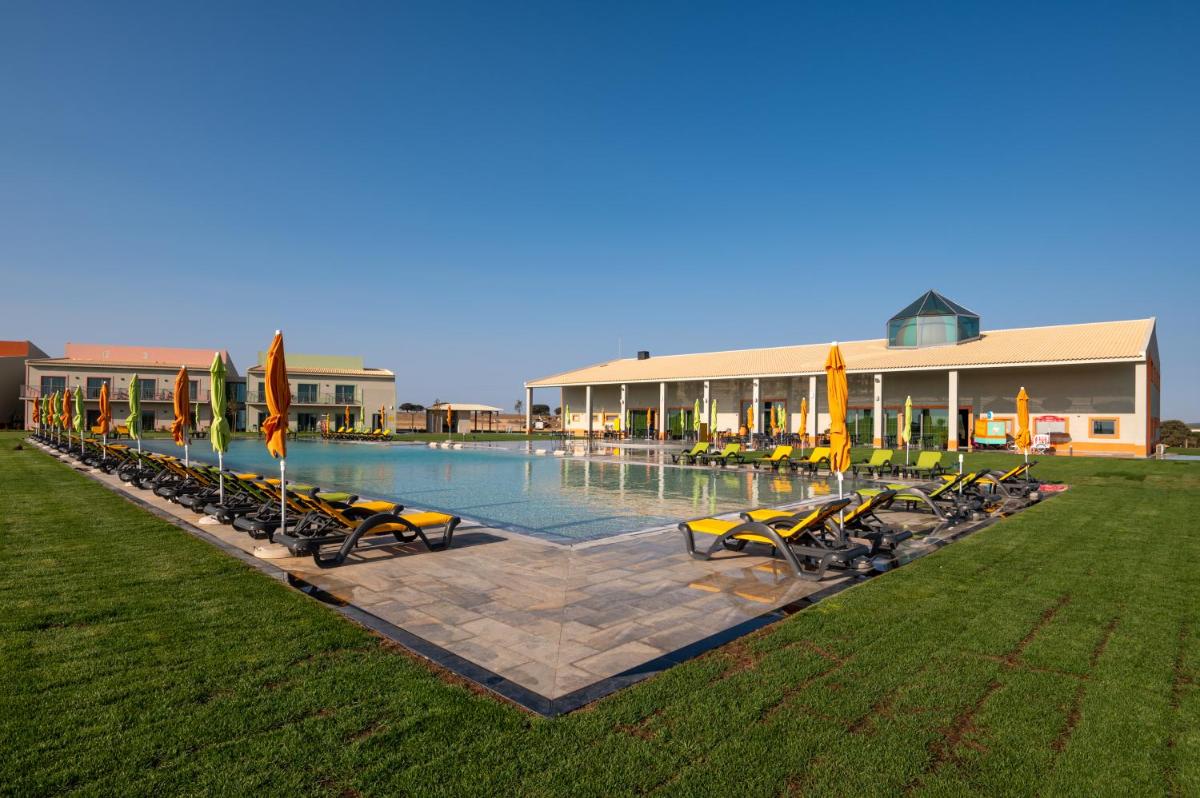 uma piscina com cadeiras e guarda-sóis ao lado de um prédio em Vila Gale Nep Kids em Beja