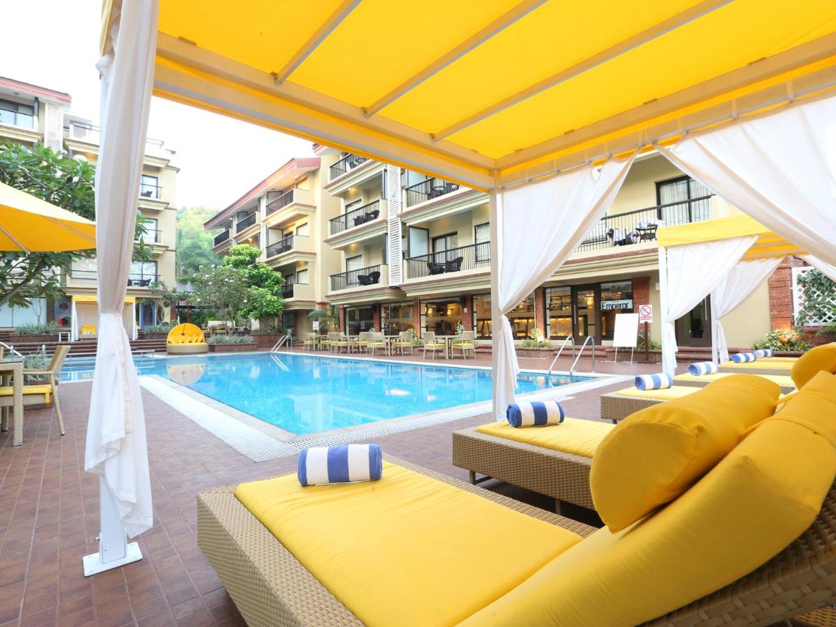a swimming pool with yellow chairs and a hotel at Deltin Suites in Candolim