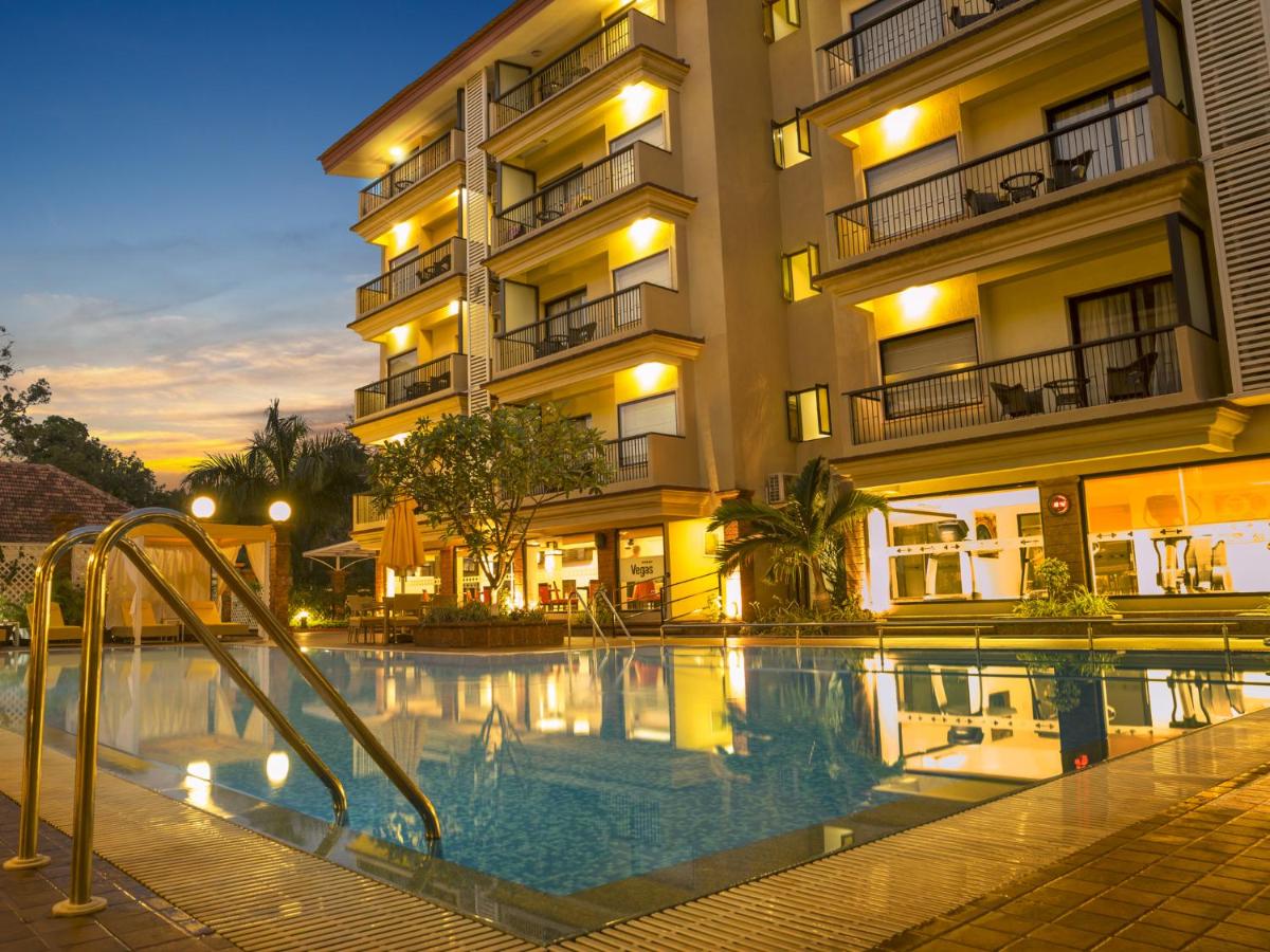 a hotel with a swimming pool in front of a building at Deltin Suites in Candolim