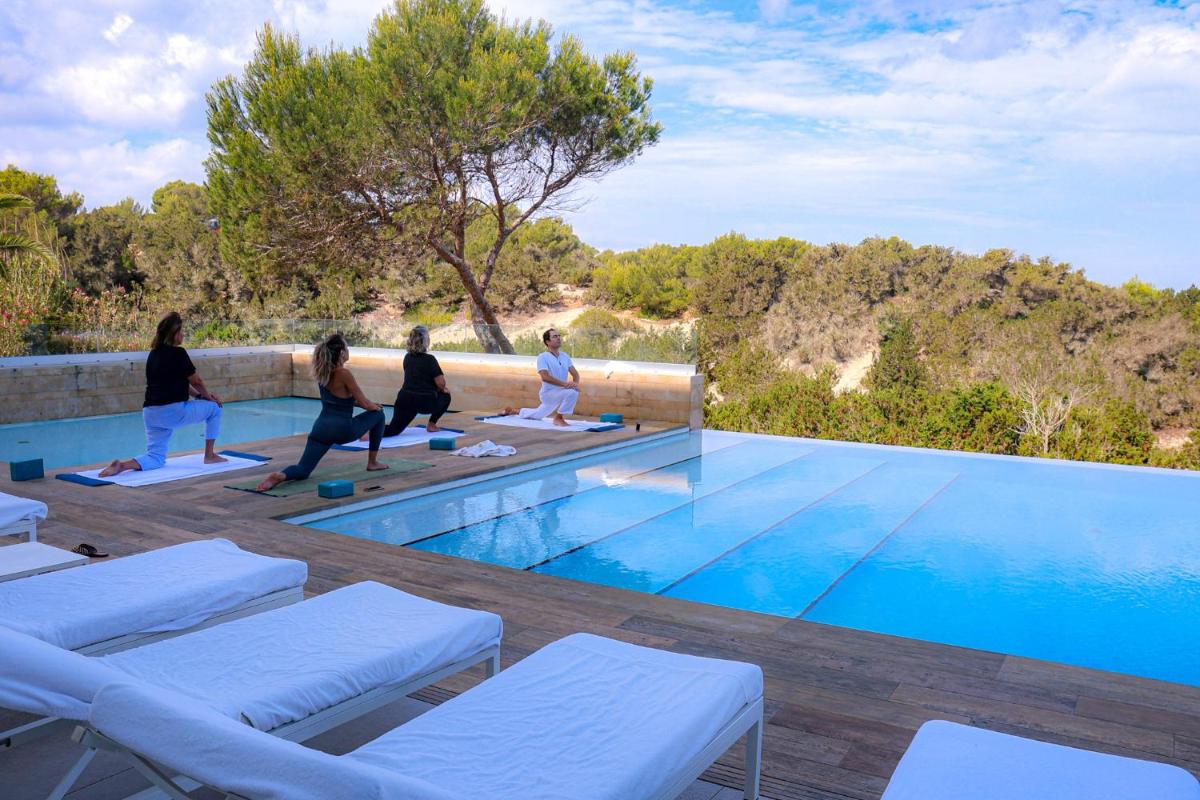 Un grupo de personas haciendo yoga junto a una piscina. en Hotel Cala Saona & Spa, en Cala Saona
