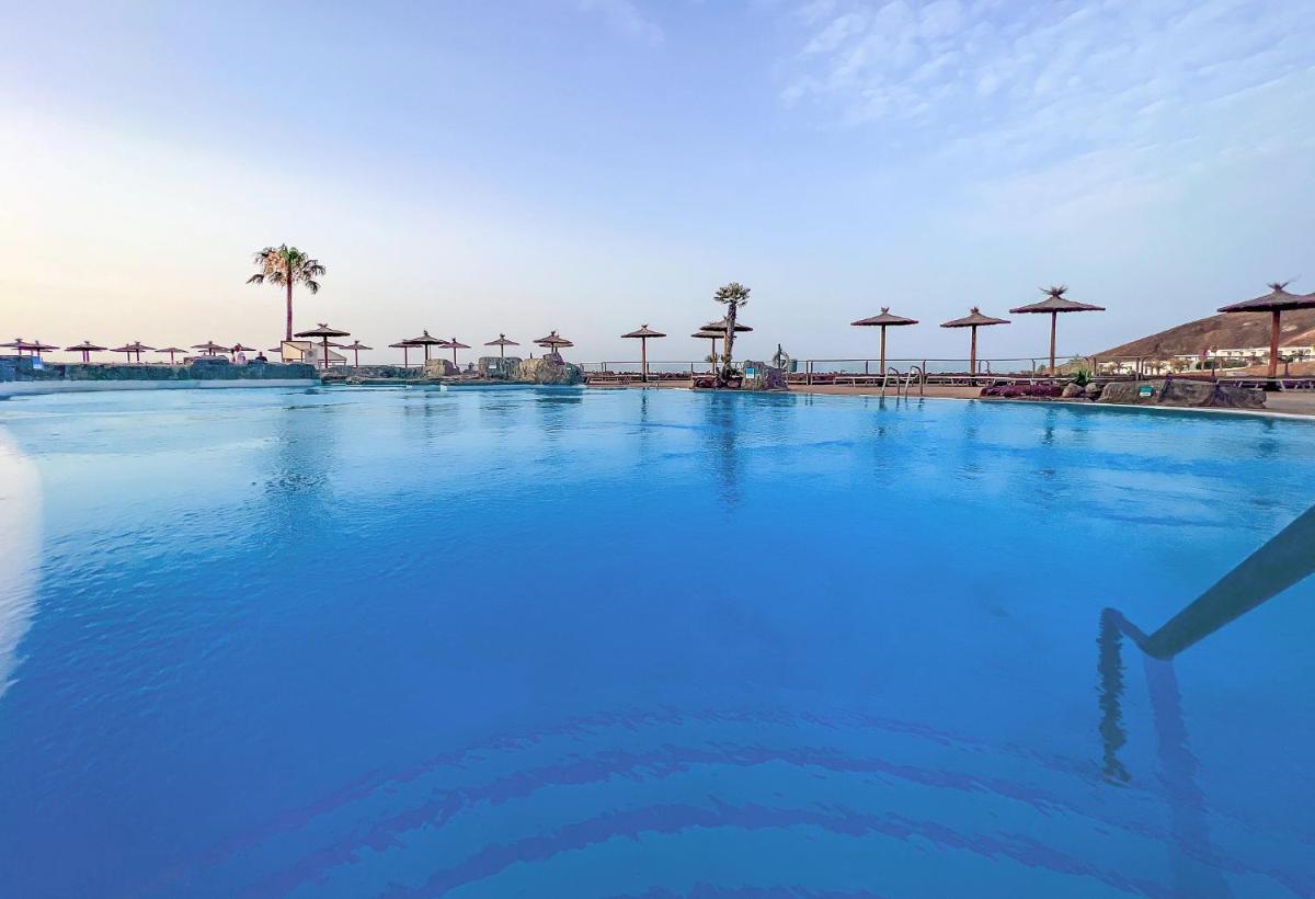 Una gran piscina con agua azul y sombrillas. en Alua Village Fuerteventura - All Inclusive, en Playa de Jandía
