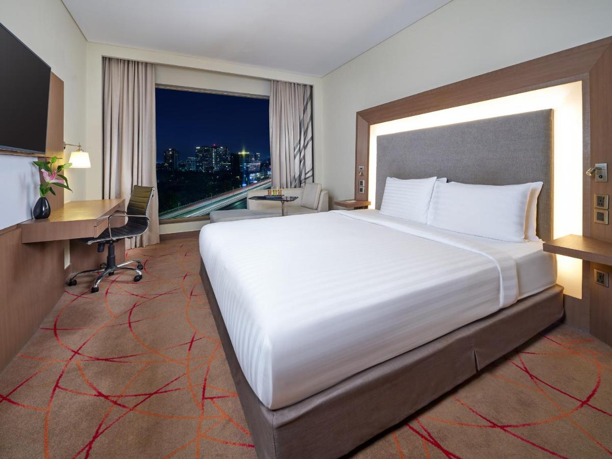 a bedroom with a large bed and a desk and a window at Novotel Ahmedabad in Ahmedabad