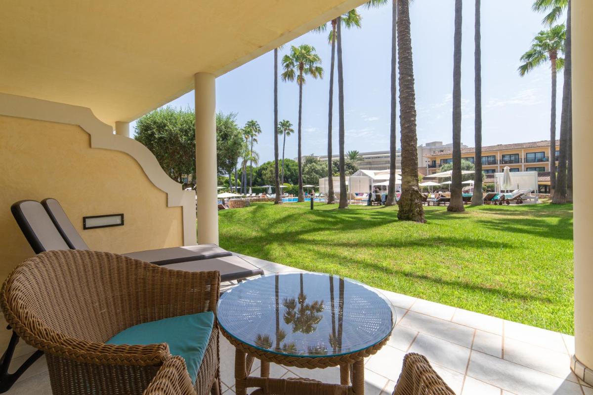 Un patio con mesa y sillas y palmeras. en CM Mallorca Palace - Only Adults, en Sa Coma