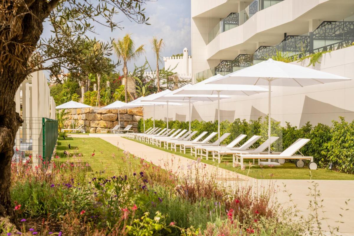 Una fila de sillas blancas y sombrillas frente a un edificio. en Eurostars Oasis Marbella, en Marbella