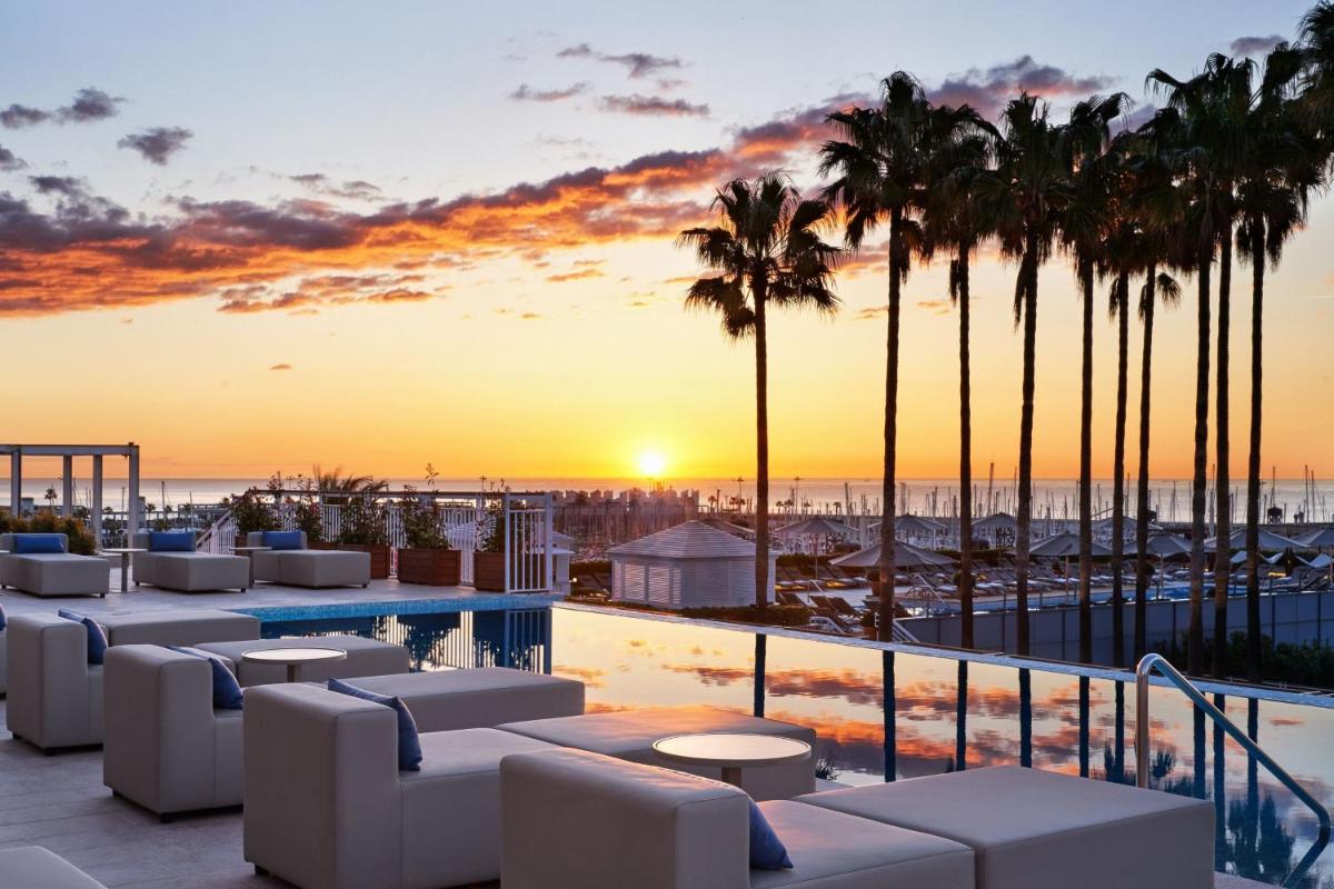 un complejo con piscina y palmeras al atardecer en Hotel Arts Barcelona, en Barcelona