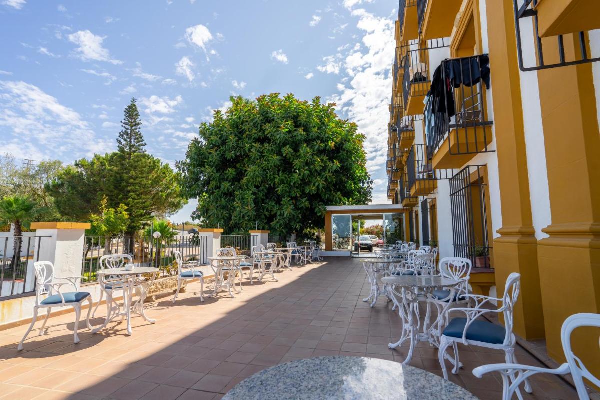Un patio con sillas y mesas blancas en un edificio. en Hotel Balneario de Chiclana, en Chiclana de la Frontera