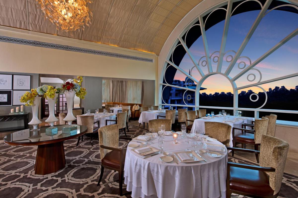 a dining room with tables and chairs and a large window at The Leela Palace Bengaluru in Bengaluru a dining room with tables and chairs and a large window at The Leela Palace Bengaluru in Bengaluru