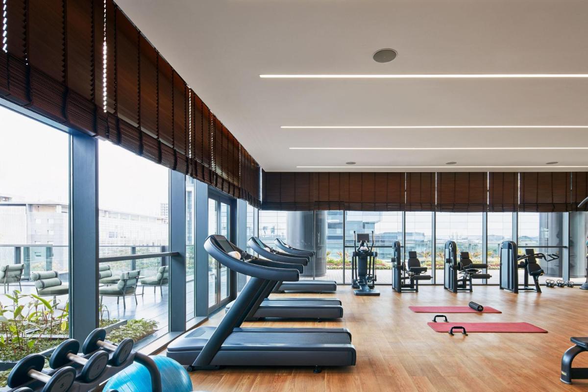 a gym with cardio equipment and large windows at The Ritz-Carlton, Pune in Pune