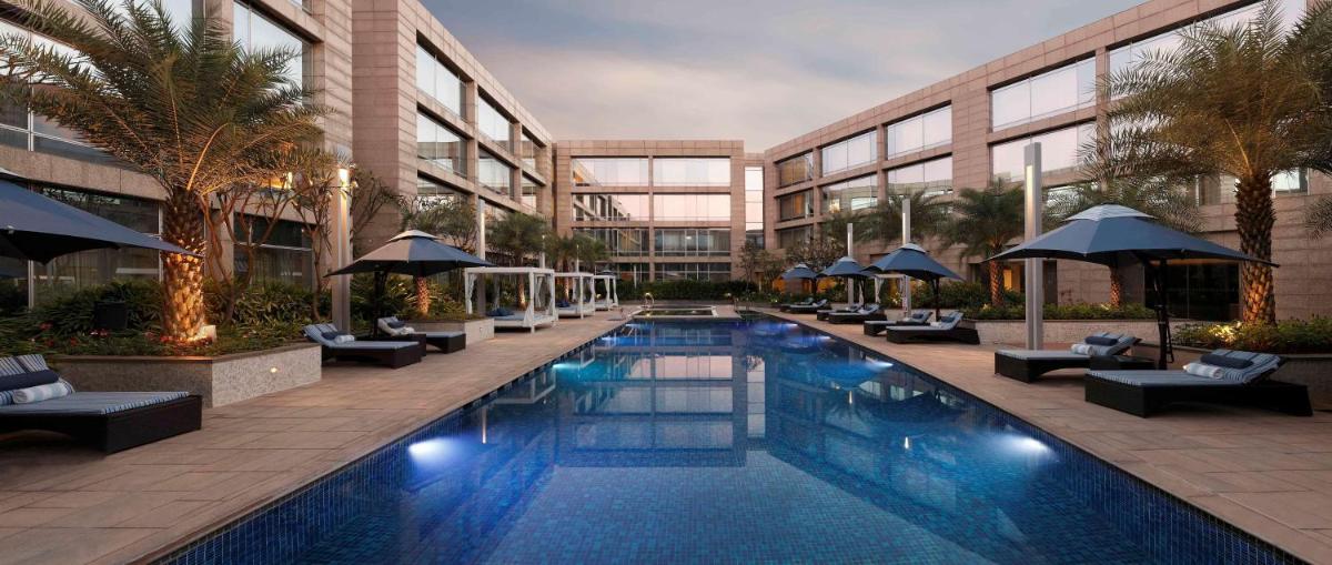 a swimming pool with chairs and umbrellas next to a building at Hilton Bangalore Embassy GolfLinks in Bengaluru