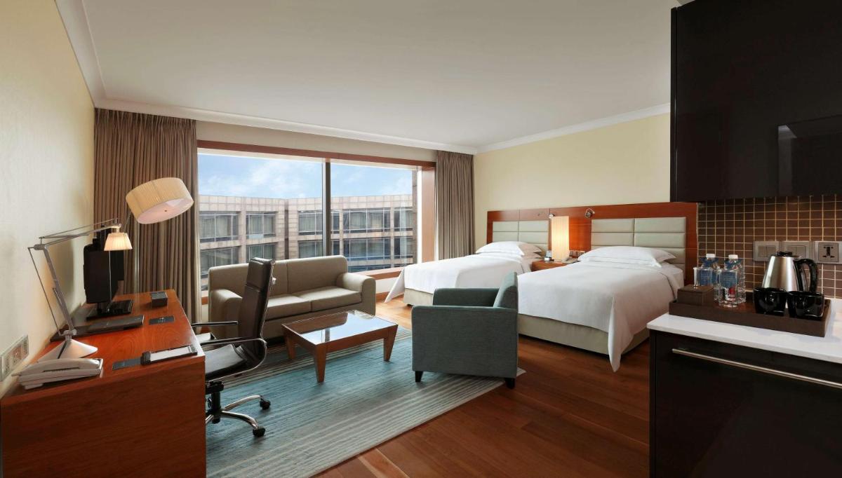 a hotel room with a bedroom with two beds and a desk at Hilton Bangalore Embassy GolfLinks in Bengaluru