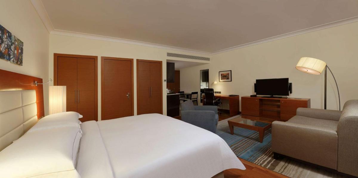 a bedroom with a white bed and a living room at Hilton Bangalore Embassy GolfLinks in Bengaluru