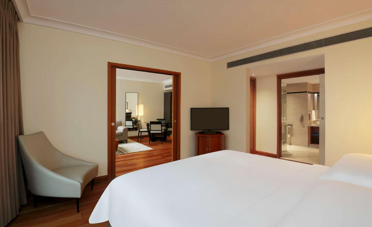 a bedroom with a white bed and a chair and a television at Hilton Bangalore Embassy GolfLinks in Bengaluru