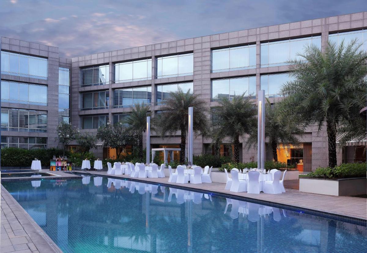 a swimming pool with white chairs in front of a building at Hilton Bangalore Embassy GolfLinks in Bengaluru