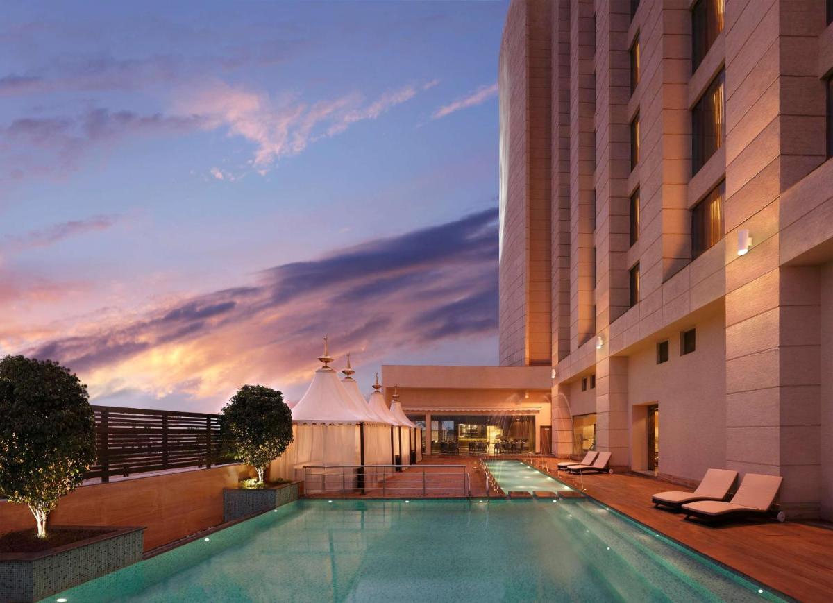 a hotel swimming pool with a sunset in the background at Hilton Jaipur in Jaipur a hotel swimming pool with a sunset in the background at Hilton Jaipur in Jaipur