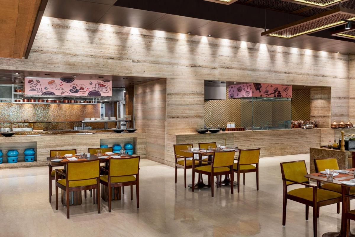 a restaurant with tables and chairs and a kitchen at Hilton Jaipur in Jaipur a restaurant with tables and chairs and a kitchen at Hilton Jaipur in Jaipur