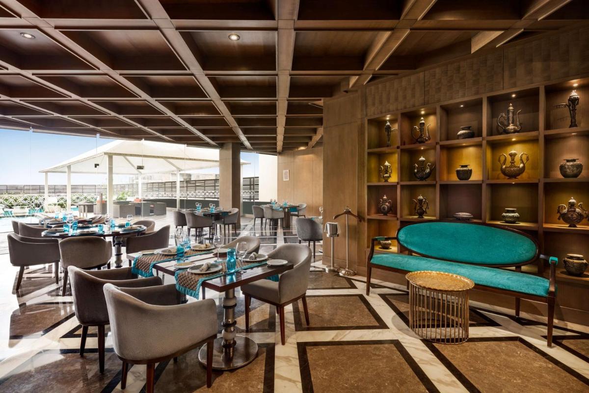 a restaurant with a green couch and tables and chairs at Hilton Jaipur in Jaipur a restaurant with a green couch and tables and chairs at Hilton Jaipur in Jaipur