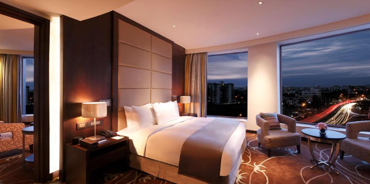 a hotel room with a bed and a large window at Hilton Jaipur in Jaipur a hotel room with a bed and a large window at Hilton Jaipur in Jaipur