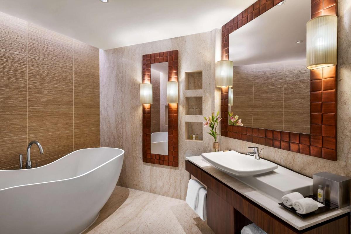 a bathroom with a tub and two sinks and a mirror at Hilton Jaipur in Jaipur a bathroom with a tub and two sinks and a mirror at Hilton Jaipur in Jaipur