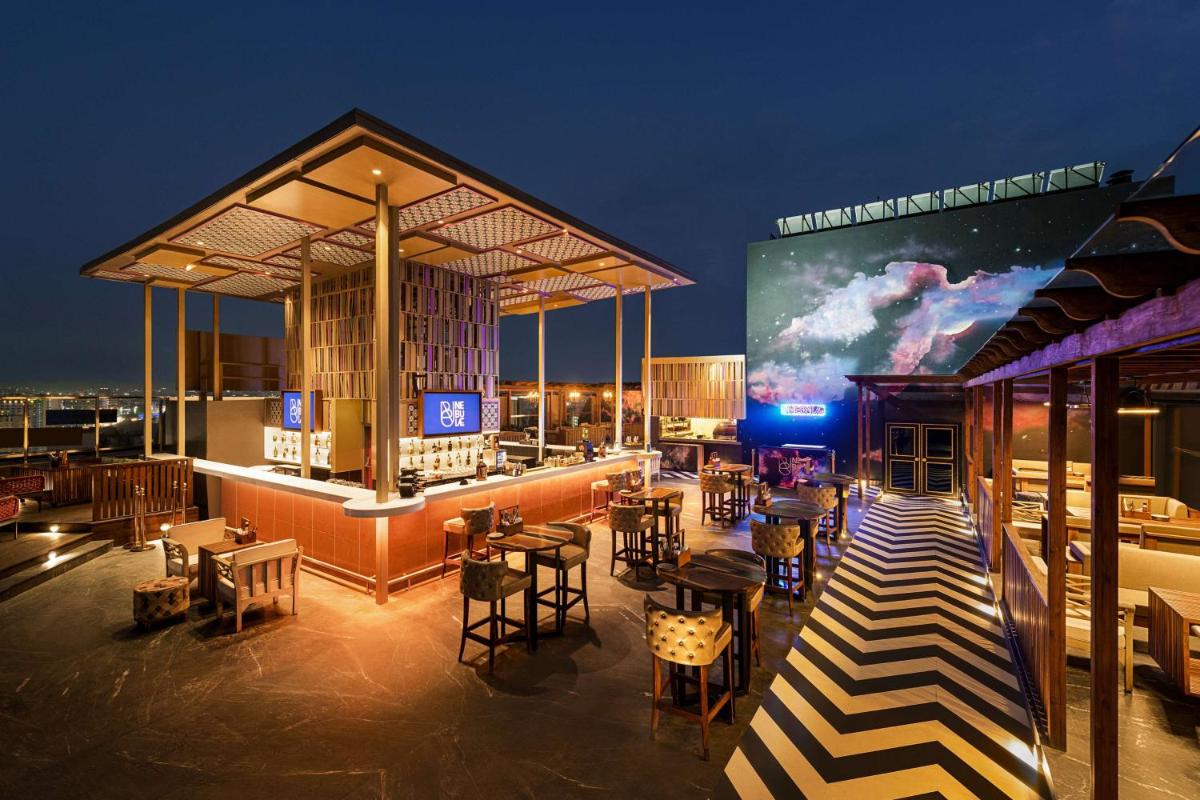 a rooftop bar with tables and chairs and a large screen at Hilton Jaipur in Jaipur a rooftop bar with tables and chairs and a large screen at Hilton Jaipur in Jaipur