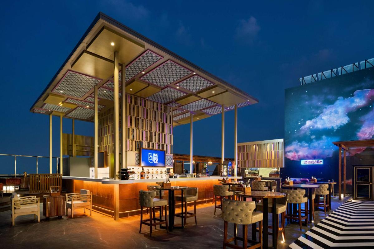 a restaurant with tables and chairs and a large screen at Hilton Jaipur in Jaipur a restaurant with tables and chairs and a large screen at Hilton Jaipur in Jaipur