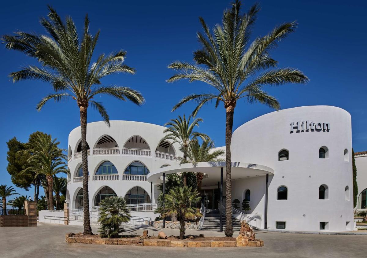 Un edificio blanco con palmeras delante. en Hilton Mallorca Galatzo, en Paguera
