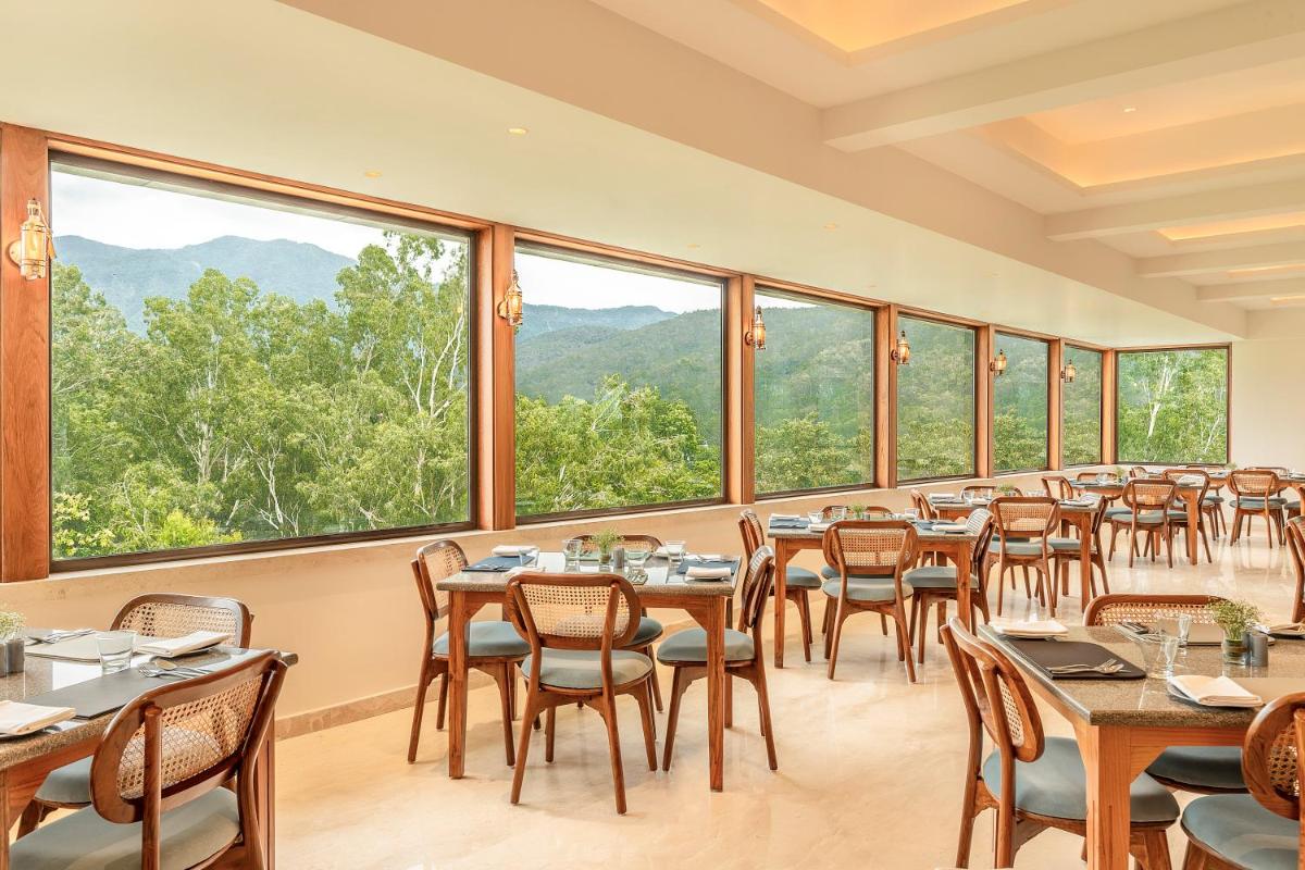 a dining room with tables and chairs and large windows at The Prominence Mussoorie Road Dehradun in Dehradun