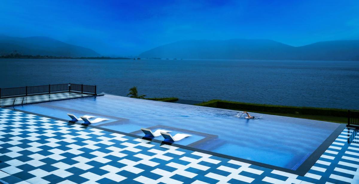 a large swimming pool with a view of the water at ZANA Lakeview Resort - most scenic lakeside resort in Udaipur