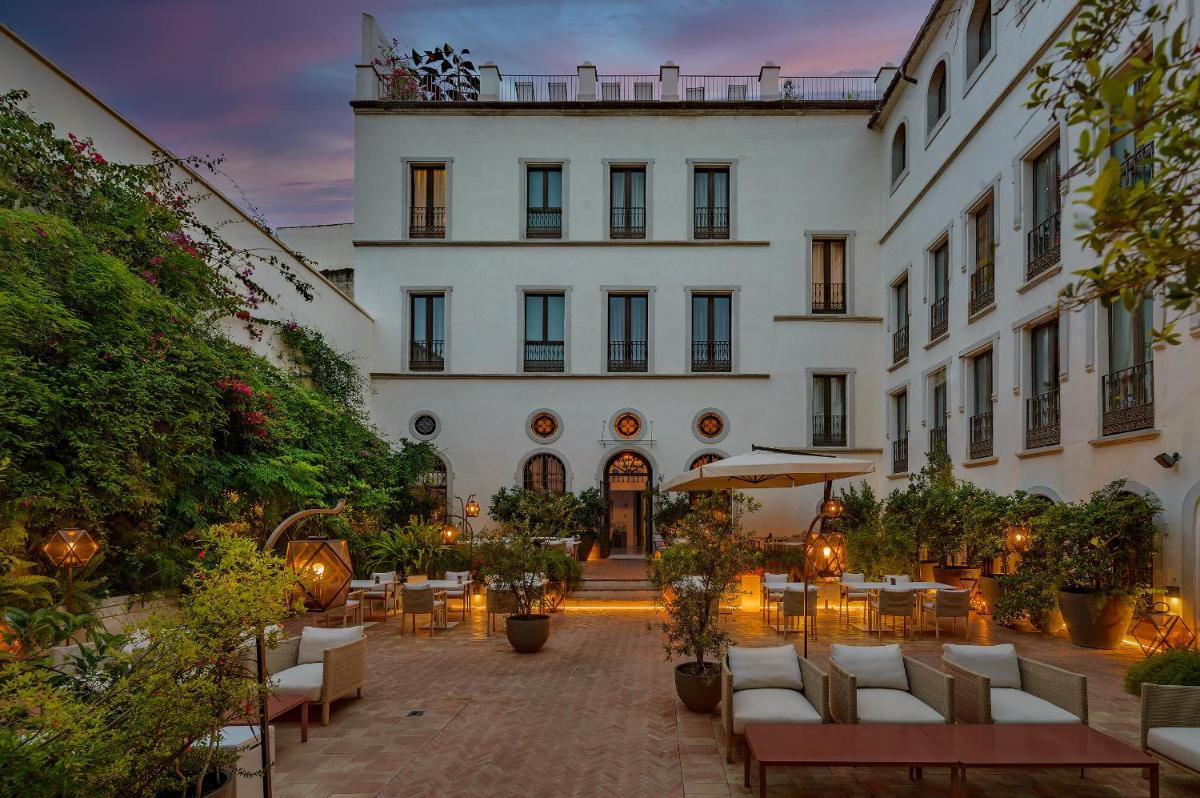 Un hotel con mesas y sillas frente a un edificio. en CoolRooms Palacio Villapanés 5 GL, en Sevilla