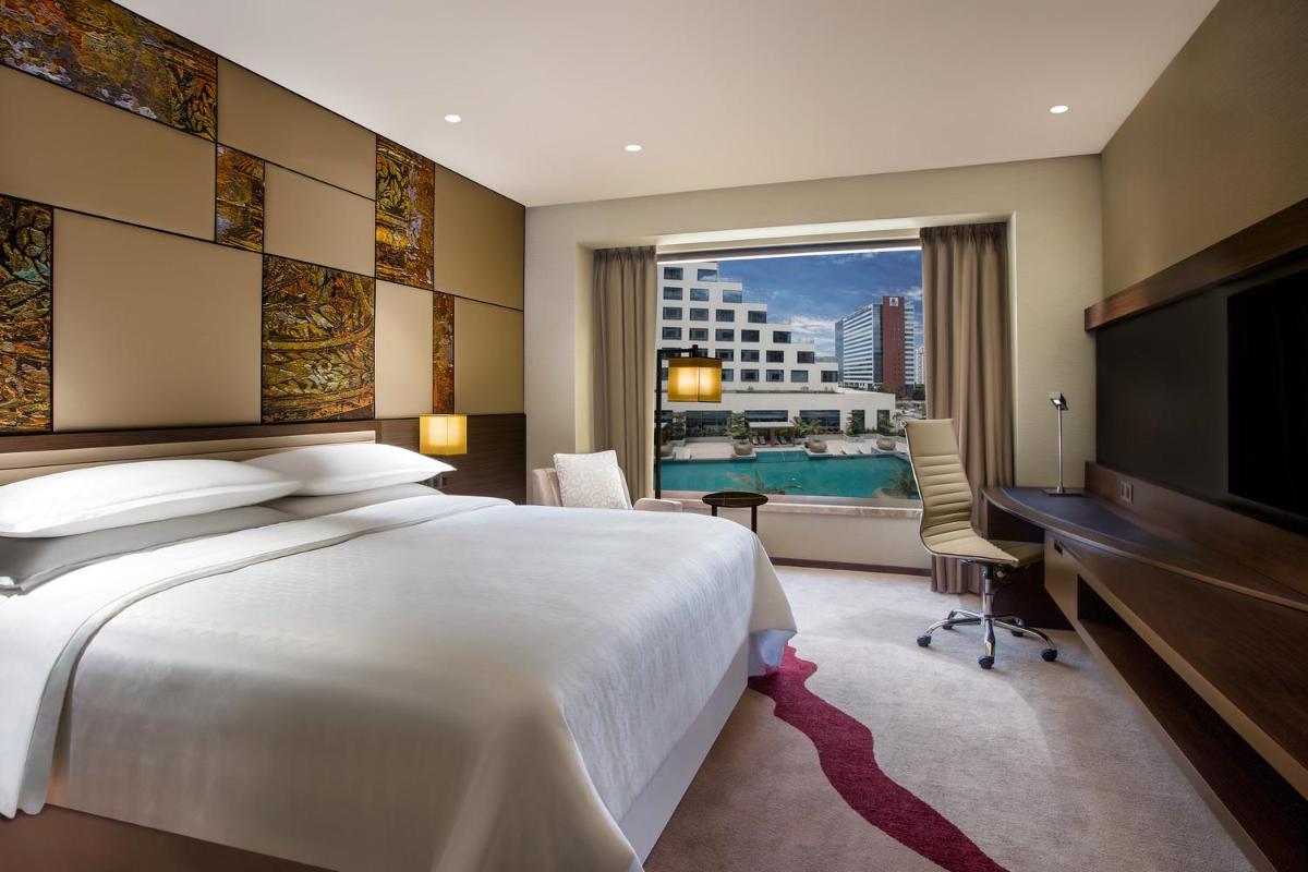 a bedroom with a bed and a desk and a television at Sheraton Grand Bengaluru Whitefield Hotel & Convention Center in Bengaluru a bedroom with a bed and a desk and a television at Sheraton Grand Bengaluru Whitefield Hotel & Convention Center in Bengaluru