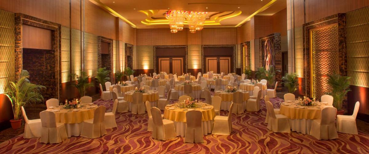 a banquet hall with white tables and chairs and a chandelier at Radisson Blu Hotel, Indore in Indore