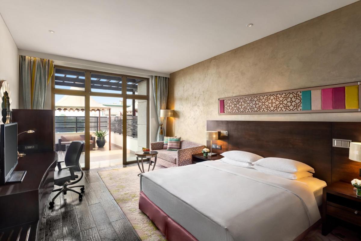 a bedroom with a large bed and a desk and a room at Hilton Jaipur in Jaipur a bedroom with a large bed and a desk and a room at Hilton Jaipur in Jaipur