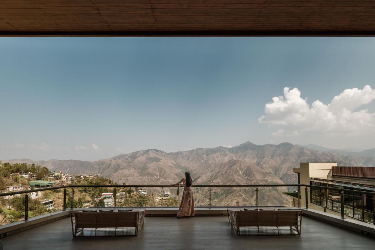 a woman standing on a balcony looking out at the mountains at JW Marriott Mussoorie Walnut Grove Resort & Spa in Mussoorie