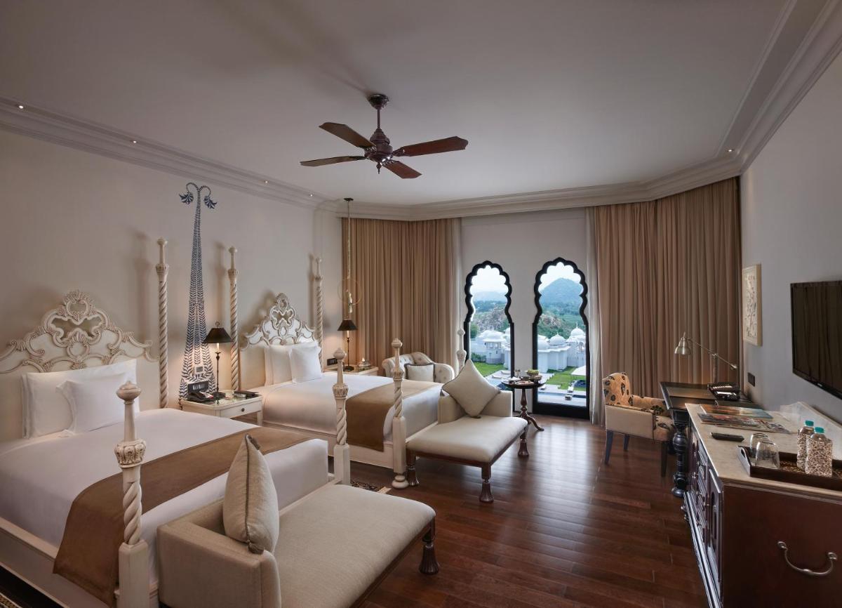 a bedroom with two beds and chairs and a ceiling fan at Fairmont Jaipur in Jaipur