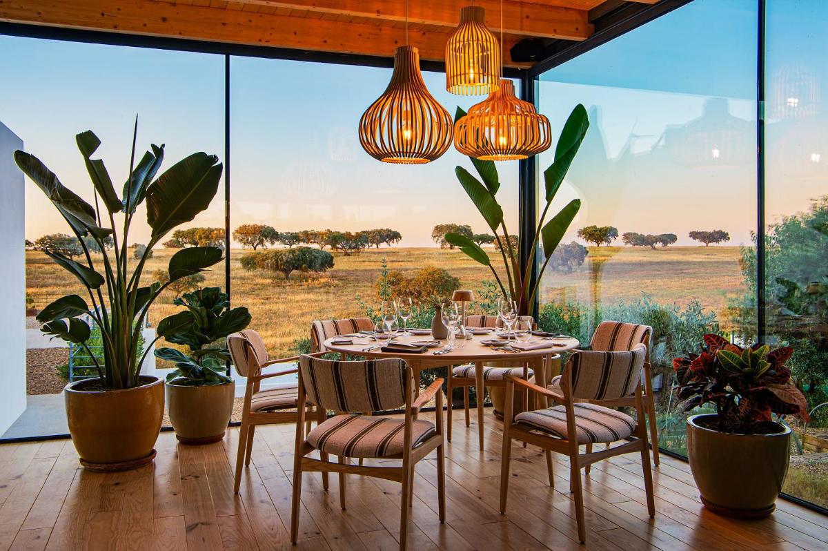 uma sala de jantar com mesa e cadeiras e janelas grandes em Herdade da Malhadinha Nova - Relais & Châteaux em Albernoa