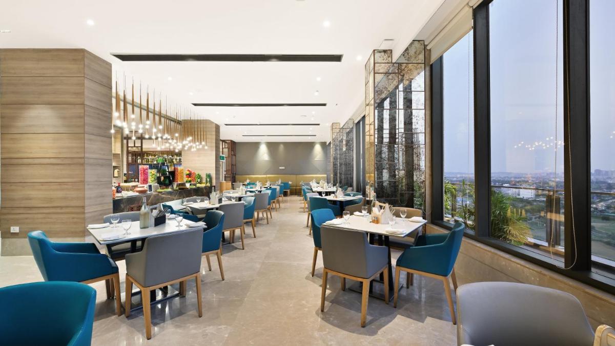 a restaurant with tables and chairs and large windows at Holiday Inn Gurugram Sector 90 by IHG in Gurgaon