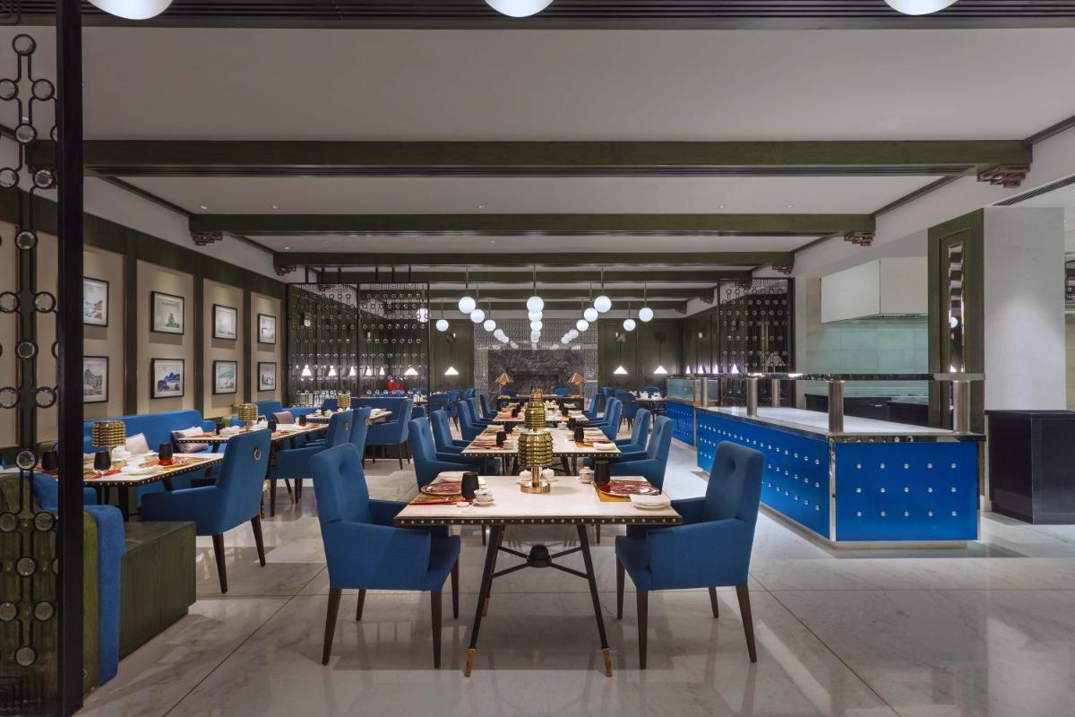 a long dining room with tables and blue chairs at ITC Narmada, a Luxury Collection Hotel, Ahmedabad in Ahmedabad