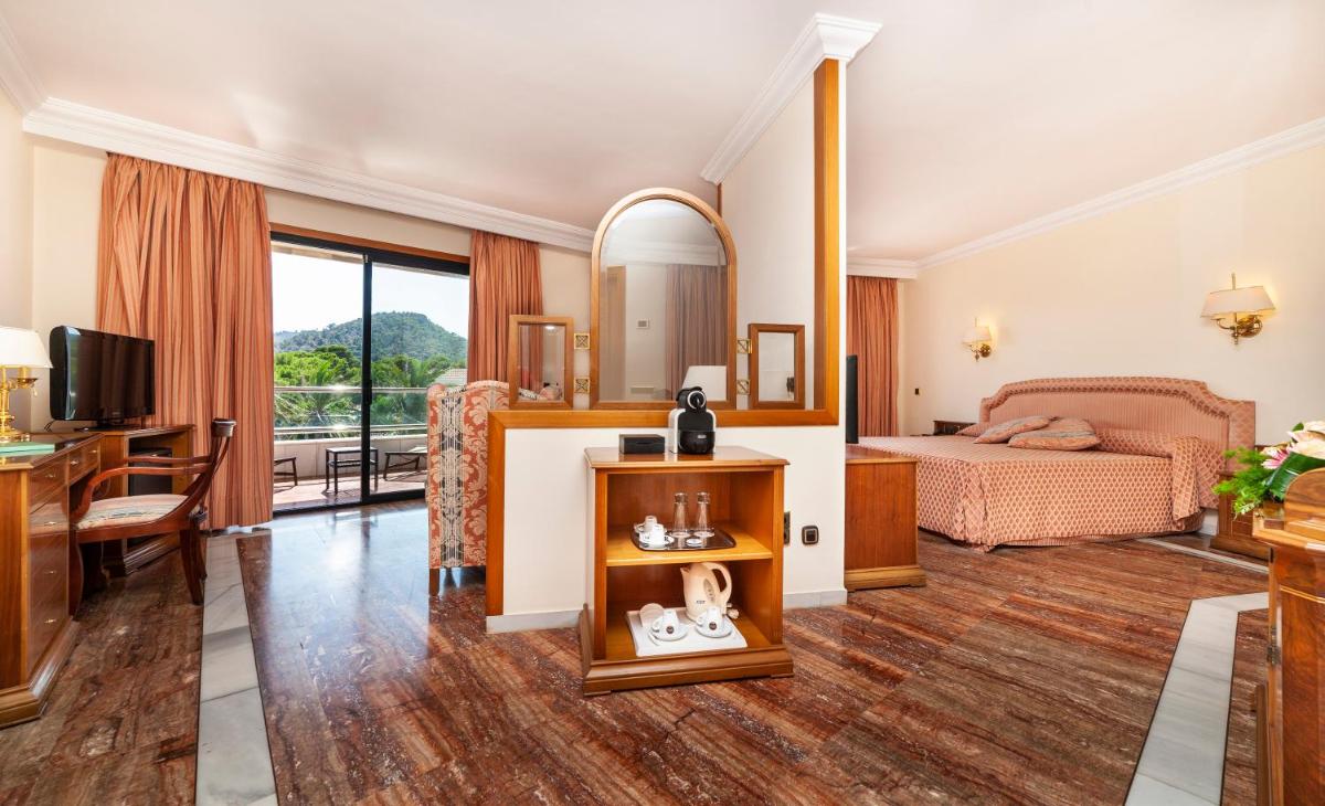 Una habitación de hotel con un dormitorio con una cama y un escritorio. en Hotel Serrano Palace, en Cala Ratjada