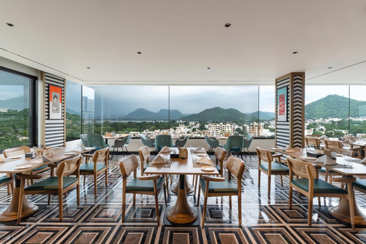 a restaurant with tables and chairs and large windows at Parallel Hotel Udaipur, a member of Radisson Individuals in Udaipur
