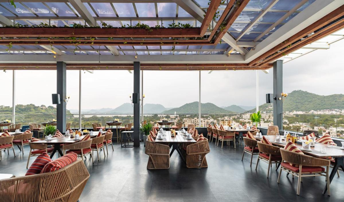 a restaurant with tables and chairs with mountains in the background at Parallel Hotel Udaipur, a member of Radisson Individuals in Udaipur