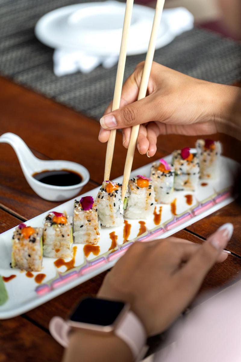 a person holding chopsticks with sushi on a plate at Parallel Hotel Udaipur, a member of Radisson Individuals in Udaipur