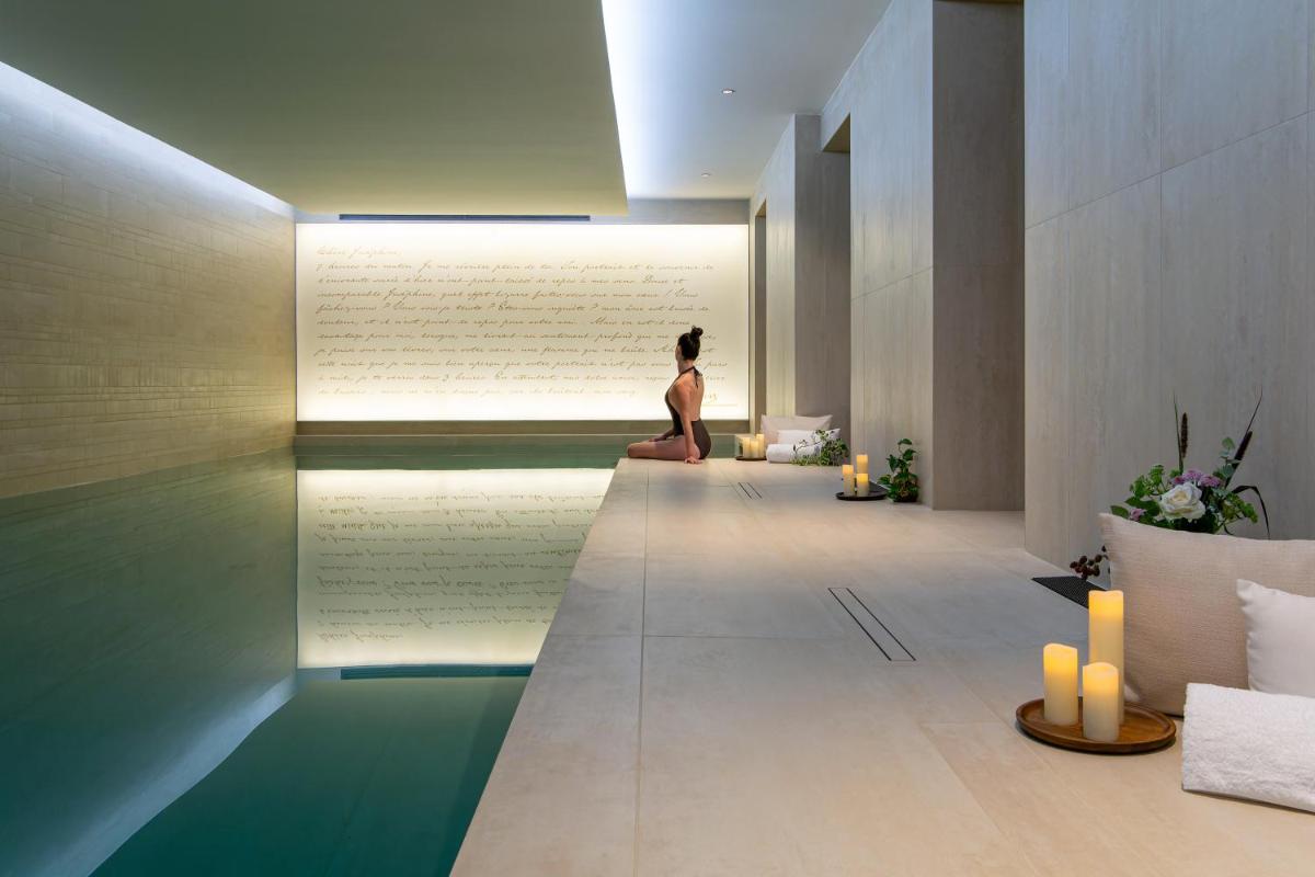 une femme assise au bord d'une piscine dans une pièce dans l'établissement Hôtel & SPA Napoléon, à Fontainebleau