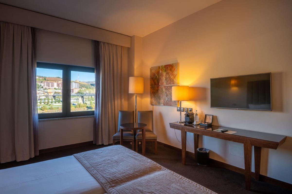 um quarto de hotel com uma cama, uma escrivaninha e uma janela em Vila Gale Collection Douro em Lamego